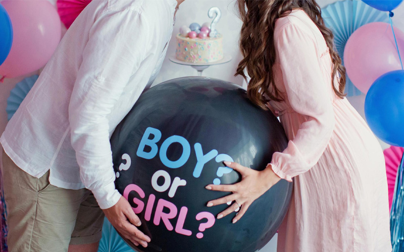 Pareja sujetando un globo negro con el mensaje Boy or Girl en una fiesta de gender reveal