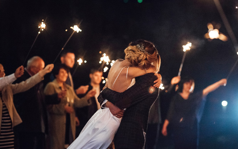 Pareja abrazándose en una fiesta postboda en Madrid con invitados y bengalas