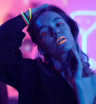 Mujer bailando en una fiesta glow con maquillaje fluorescente y luces de neón rosas y azules