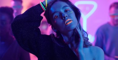 Mujer bailando en una fiesta glow con maquillaje fluorescente y luces de neón rosas y azules