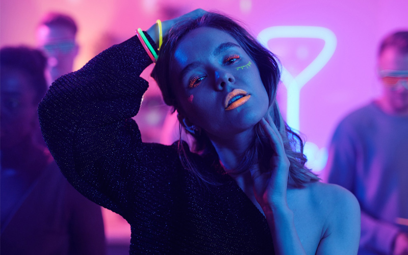 Mujer bailando en una fiesta glow con maquillaje fluorescente y luces de neón rosas y azules