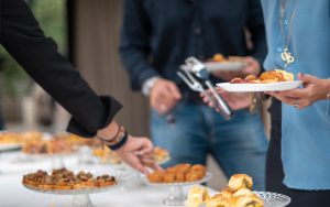 Invitados sirviéndose aperitivos de un buffet con comida para fiestas y picoteo