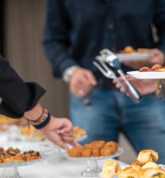 Invitados sirviéndose aperitivos de un buffet con comida para fiestas y picoteo